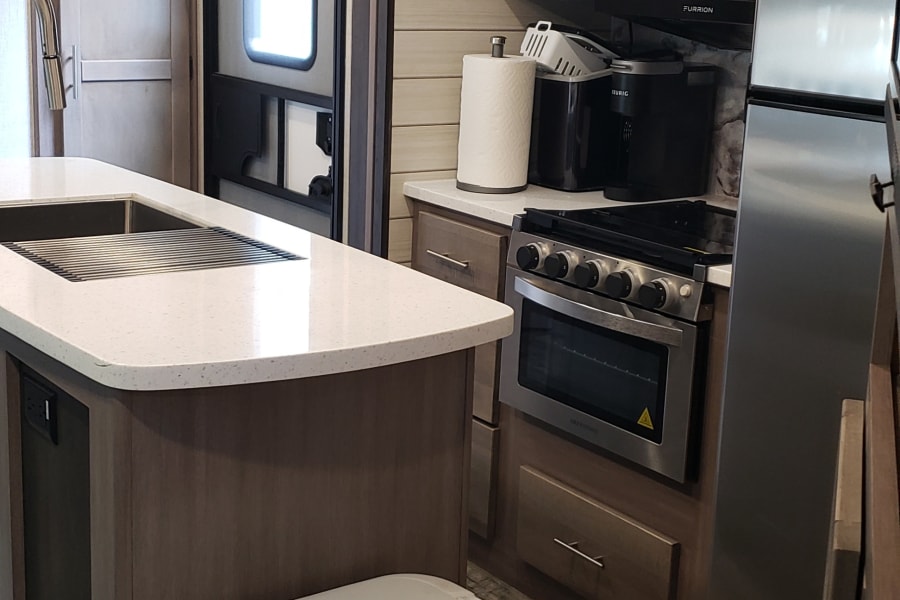 RV rental kitchen with island, sink, microwave, oven, fridge, and trash can on wood floor.