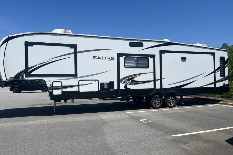 A large white and black Sabre Cobalt RV rental is parked on asphalt with a clear blue sky.