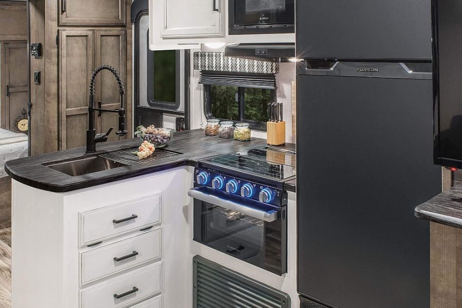 Enjoy travel convenience in this RV rental's modern kitchen: black fridge, oven, microwave, sink, and ample storage.