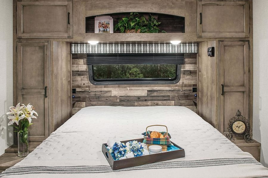 Cozy RV rental bedroom featuring a queen bed, rustic wood paneling, and built-in storage cabinets.