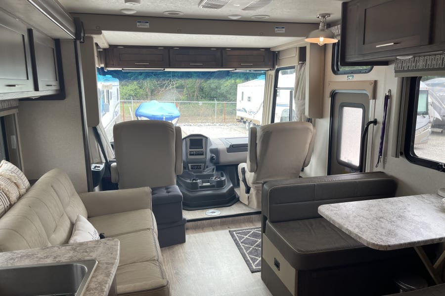 Spacious RV rental interior showing the driver's cockpit, living area with sofa, dinette, and kitchen sink.