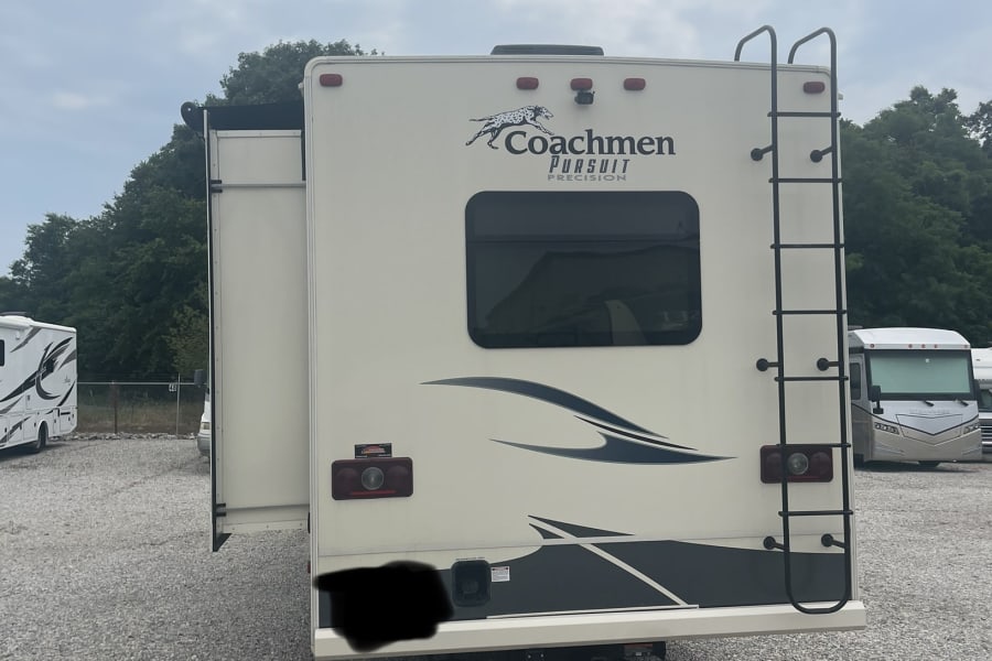 Rear view of a Coachmen Pursuit RV rental parked on a gravel lot, slide-out extended. Ideal camper for travel.
