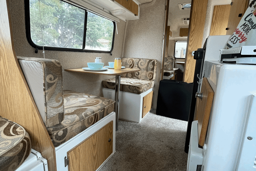 Cozy RV rental interior with dinette seating, a kitchen area, patterned cushions, and a ceiling vent.