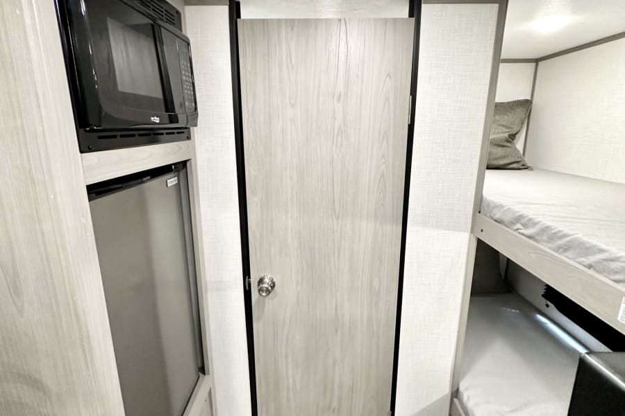 RV rental interior: compact kitchen with microwave & fridge, wooden door, and cozy bunk beds for travelers.