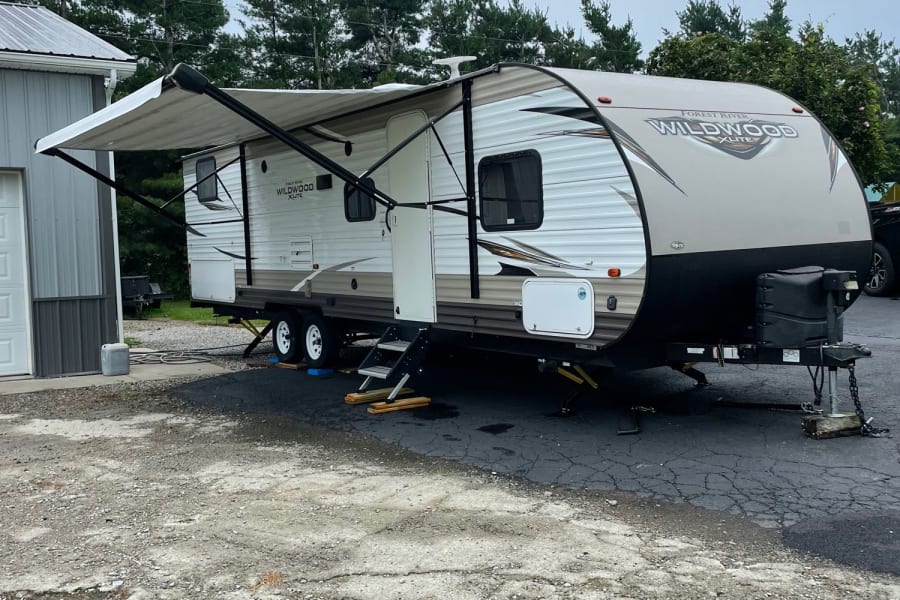 A white and tan Forest River Wildwood X-Lite travel trailer with awning extended, ready for your RV rental.