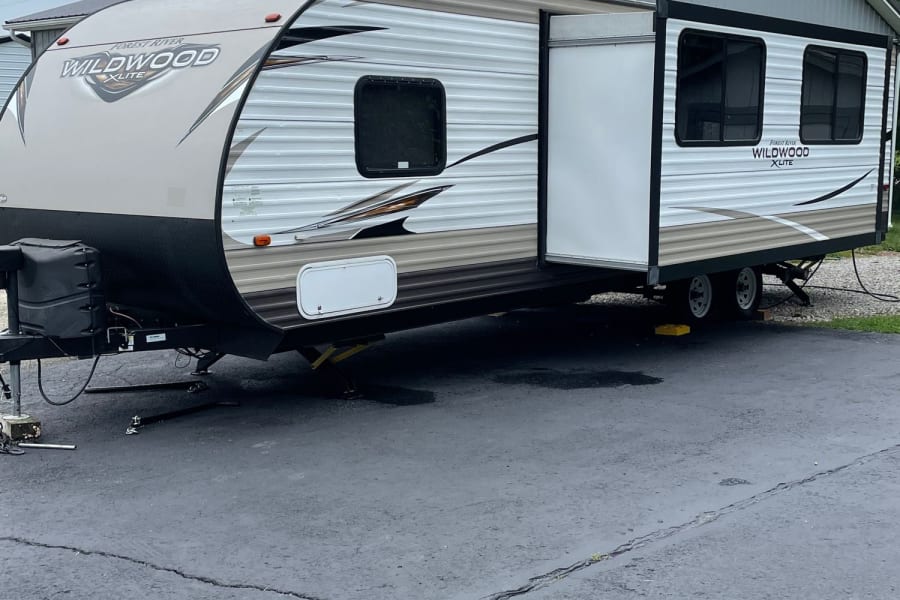 This RV rental is a Forest River Wildwood travel trailer, parked & leveled on asphalt with its slide-out extended.