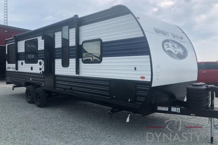 A white and blue Grey Wolf travel trailer is shown on gravel. Ideal for your next RV rental adventure!
