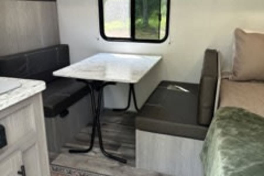 This RV rental's inviting interior features a dinette, compact kitchen, and bed area, perfect for road trips.