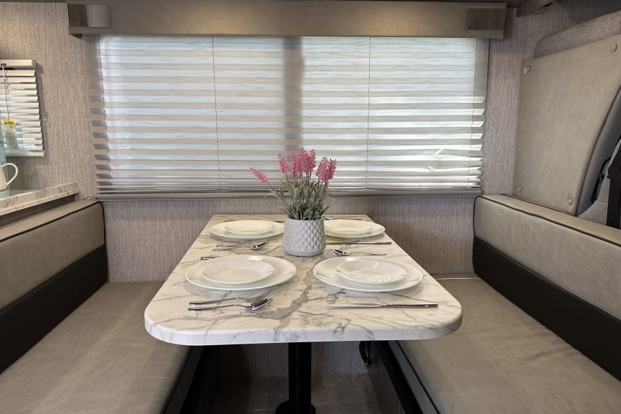 This modern RV rental interior features a comfortable dinette area with a marble table, set for four, perfect for travel.
