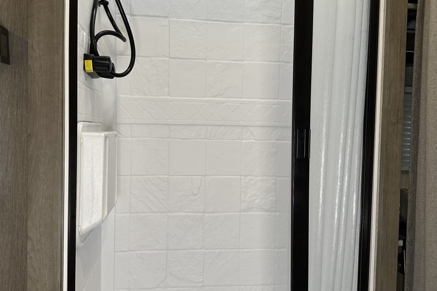 Clean shower stall in an RV rental, featuring a handheld showerhead, storage caddy, and translucent sliding door.