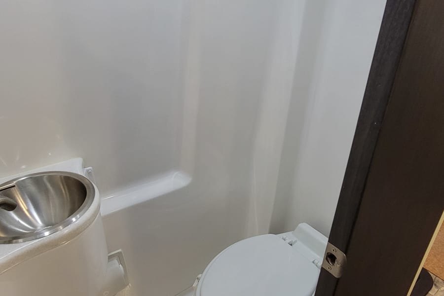 A small, white RV rental bathroom equipped with a toilet and a compact stainless steel sink.