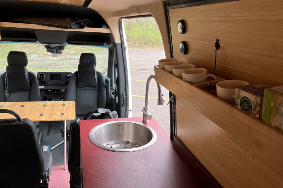 RV rental: Interior of a custom camper van featuring a kitchen sink, modular table, and smart storage.