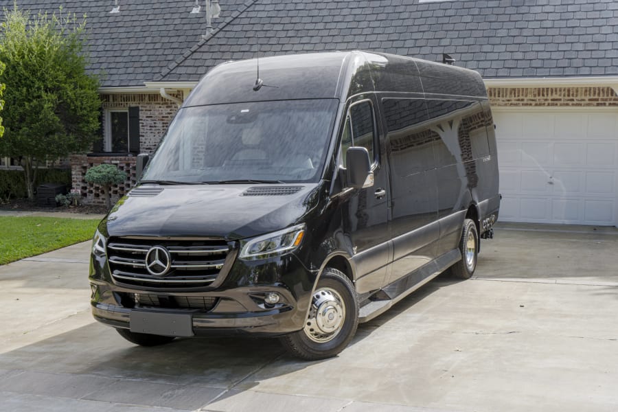 Sleek black Mercedes-Benz Sprinter van in a sunny driveway. Ideal for your next RV rental or luxury group travel adventure.