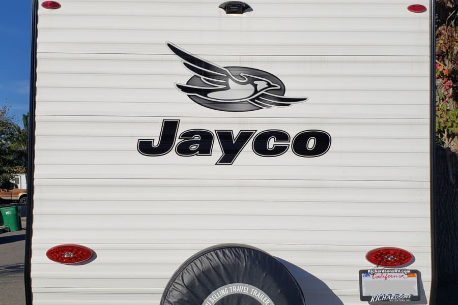White Jayco travel trailer, with its spare tire and stabilizing jacks. A great option for your next RV rental adventure.