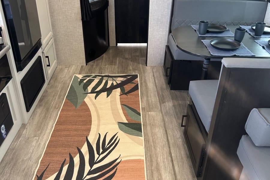 Clean RV rental interior showing a dinette, kitchen area, and bunk beds, with a patterned rug.