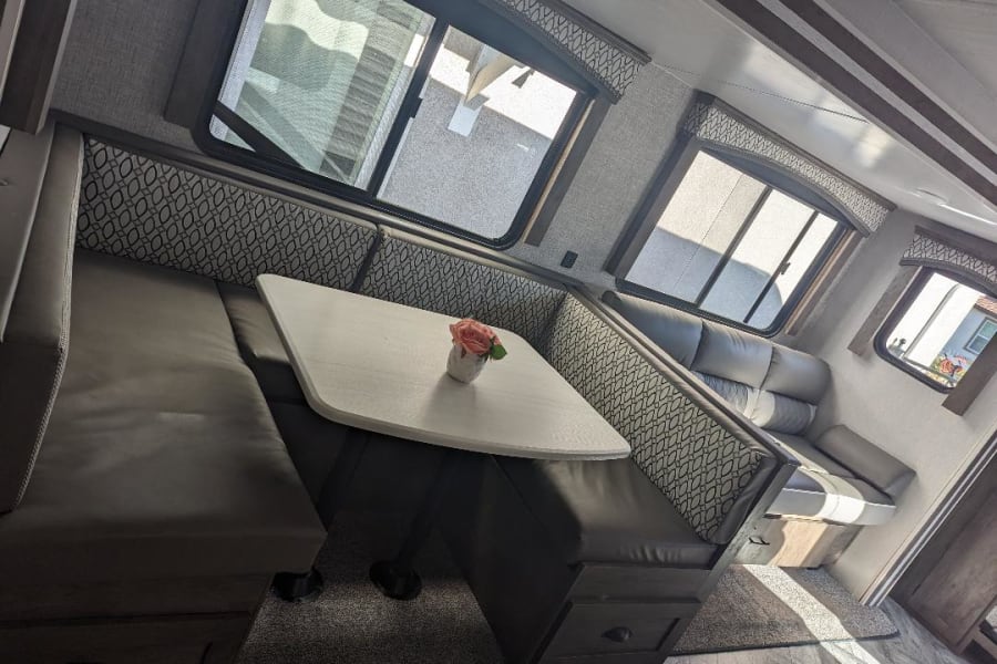 This RV rental interior features a spacious dinette, comfortable sofa, and bright windows, perfect for road trip living.