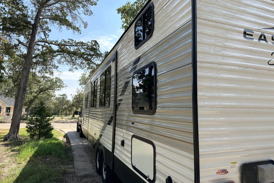 Light-colored travel trailer RV rental with windows, parked on a sunny day. Ready for your next outdoor adventure.