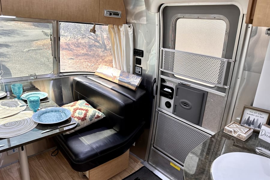 Inside a modern Airstream RV rental, showing the cozy dinette with place settings, control panel, and screen door.