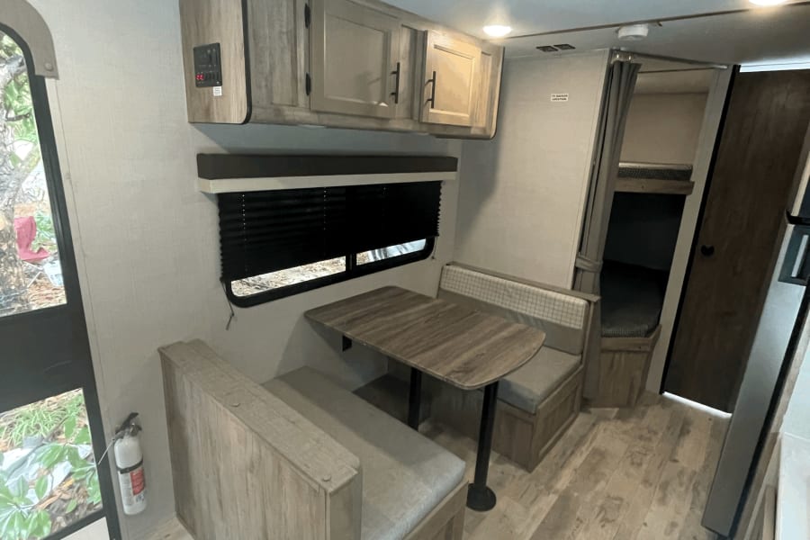 View inside an RV rental showing a dinette with booth seating, overhead cabinets, window, and bunk access.