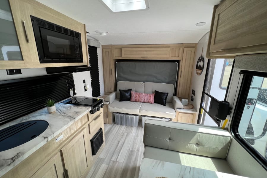 Step inside this modern RV rental! Features a compact kitchen, sofa, dining booth, and sleek light wood cabinetry.