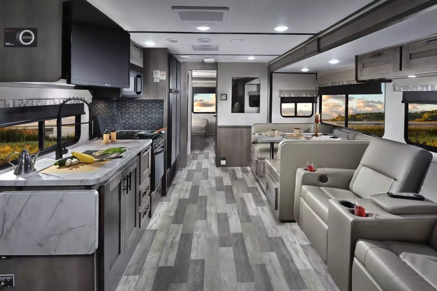 Explore this modern RV rental interior featuring a full kitchen, dining booth, comfy recliners, and bright windows.
