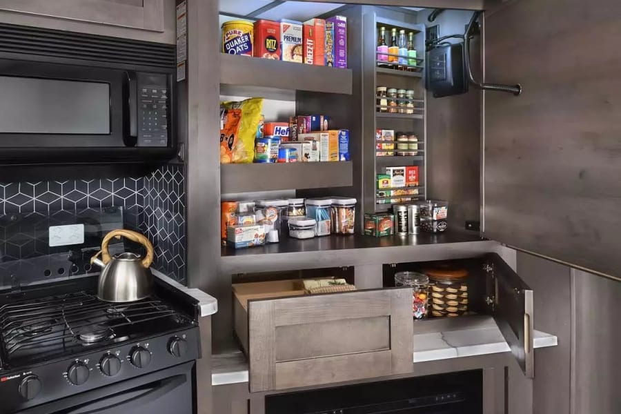 RV rental kitchen featuring an organized pantry with food, spices, and a pull-out rack, plus a microwave, stove, and fireplace.