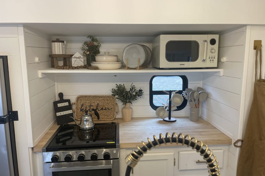 Stylish RV rental kitchen with white shiplap, open shelves, microwave, stove, and organized essentials.