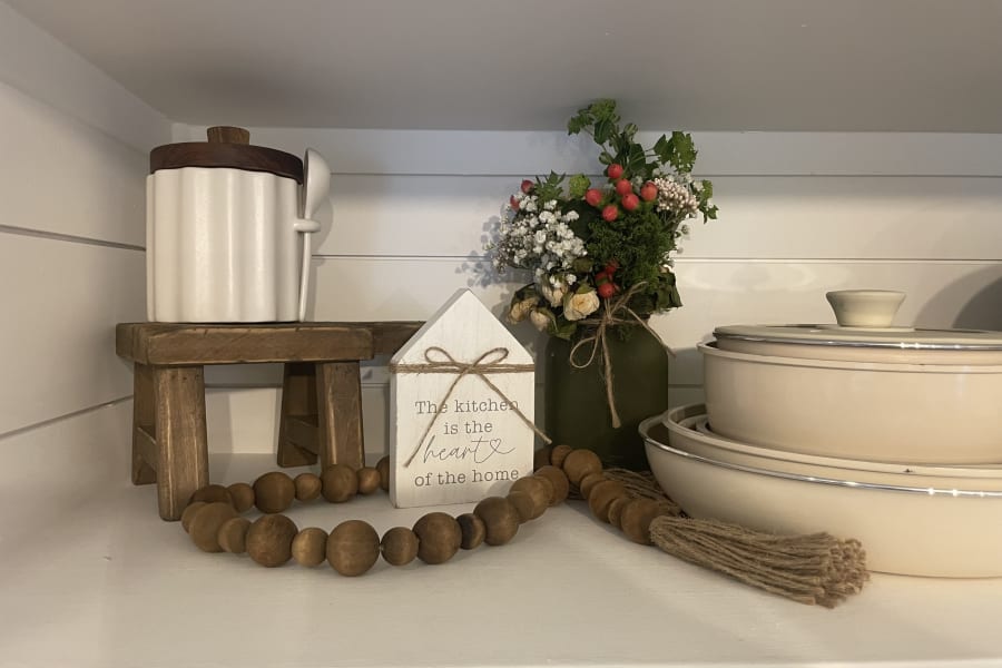 Cozy kitchen decor: white canisters, a wooden stool, floral arrangement, and mixing bowls on a shelf, great for an RV rental.