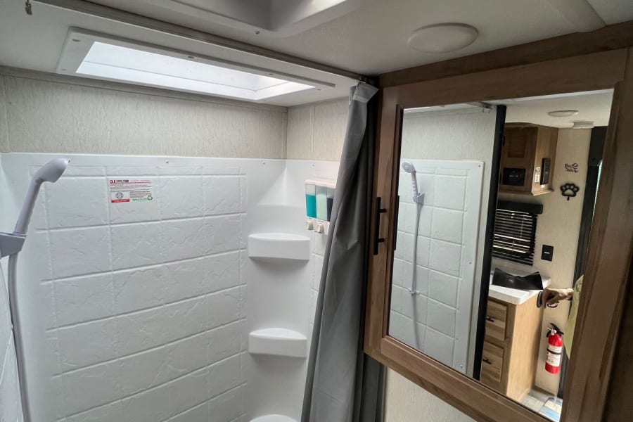 Clean RV rental bathroom. Features a white shower stall, vanity sink, mirror, and ceiling fan with skylight.