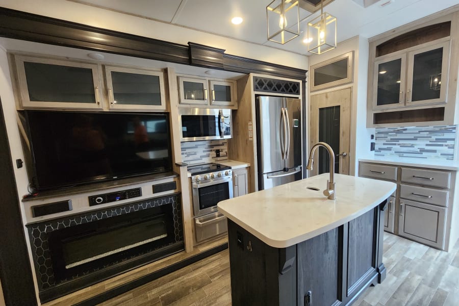 RV rental's contemporary interior: kitchen island, stainless appliances, large TV, and a modern electric fireplace.