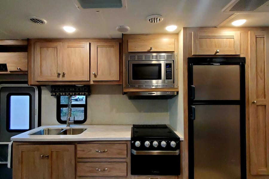 RV rental kitchen interior: bright with skylight, featuring wood cabinets, sink, microwave, range, and refrigerator.