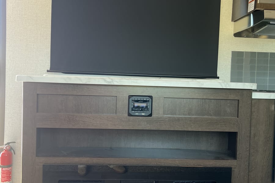 This RV rental offers a well-equipped living area with a large TV, Jensen control panel, and vibrant electric fireplace.