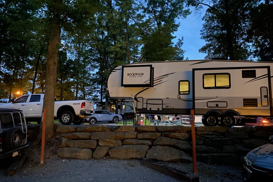 Rockwood Ultra Lite RV rental parked at a serene evening campsite with trucks and cars surrounded by trees.
