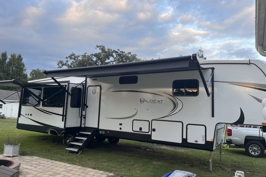 A large white Wildcat RV, a perfect rv rental, parked on grass with awnings extended and steps down, ready for use.