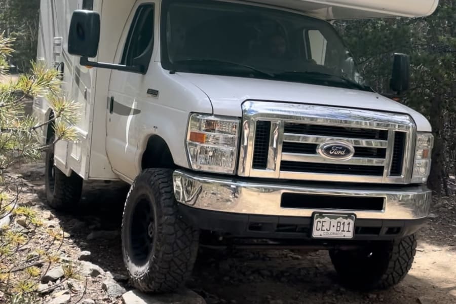 A white Majestic RV rental, a lifted Class C, navigates a rugged, rocky Colorado trail. Built for off-road adventures!