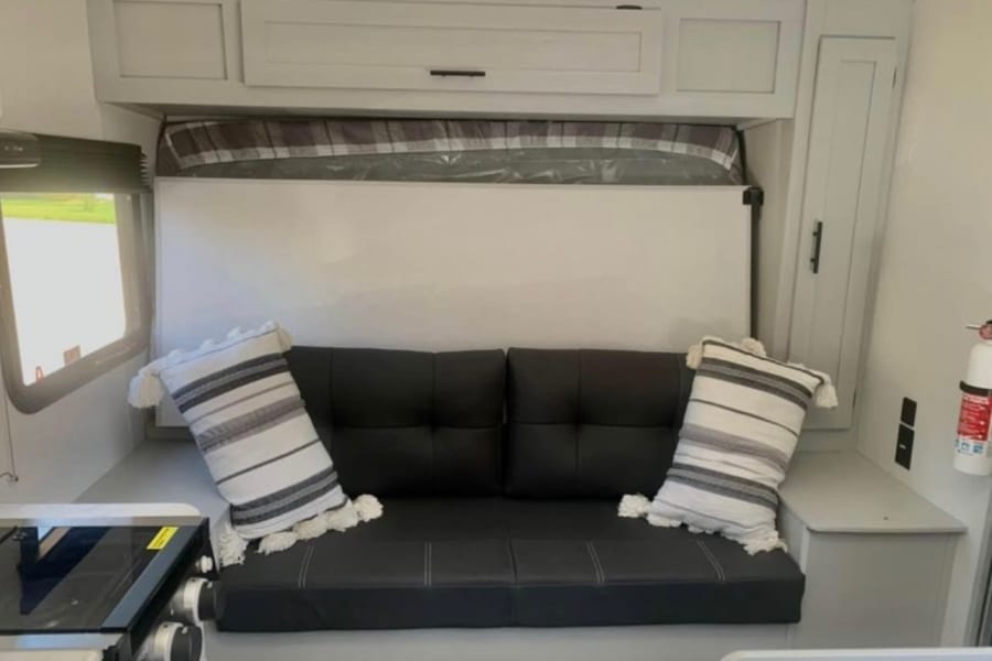 RV rental interior: a black sofa converts to a bed under white cabinets. Features a compact kitchen & window.