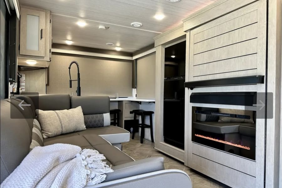 Cozy RV rental living area featuring a modern kitchen, comfortable sectional, and electric fireplace for your next adventure.