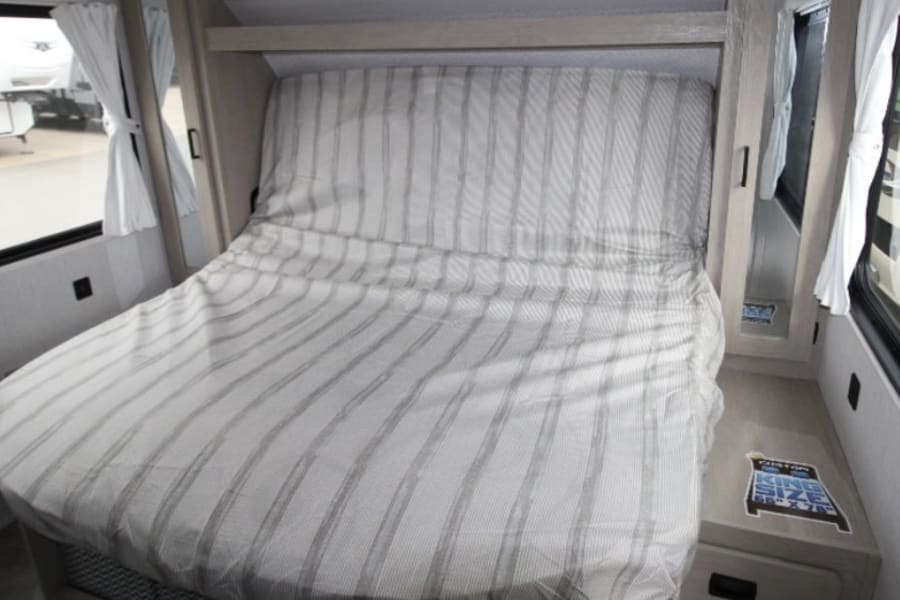 Cozy RV rental bedroom with striped bed, windows, and built-in storage, ideal for compact living.