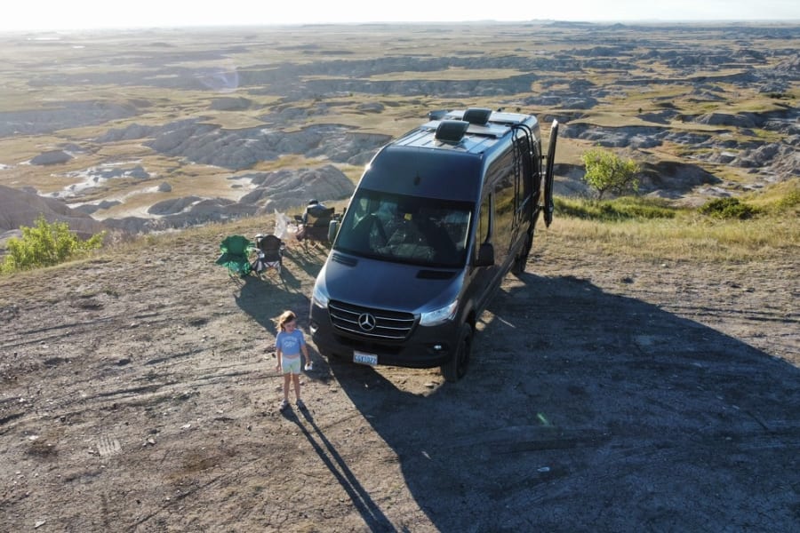 Experience stunning views with an RV rental! This camper van is parked overlooking badlands, with a child enjoying the vast landscape.