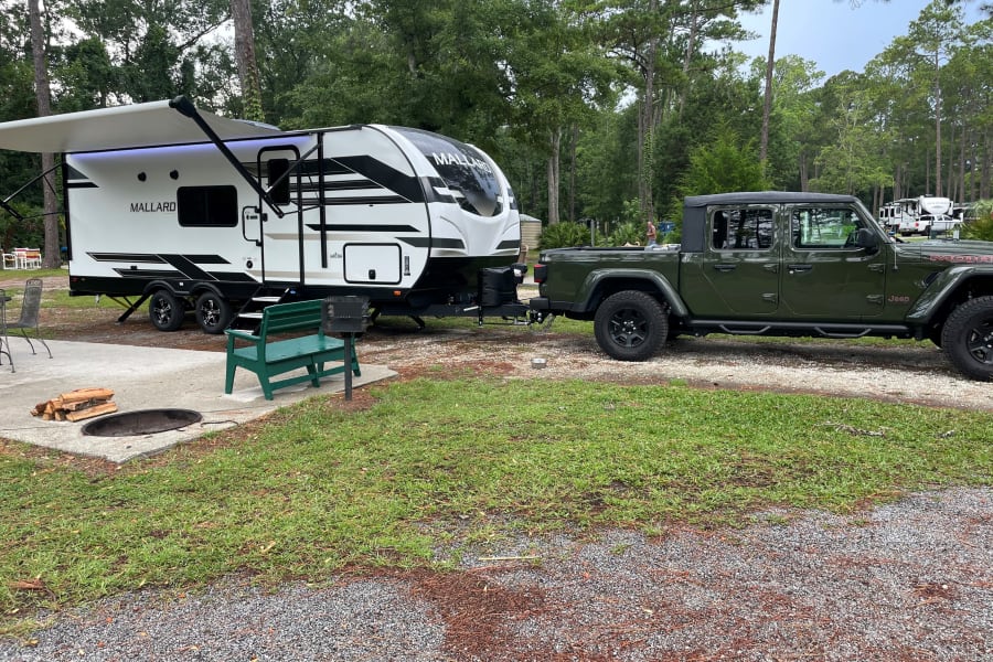 Mallard travel trailer and Jeep Gladiator at a spacious campsite, ready for your next RV rental adventure with a fire pit.