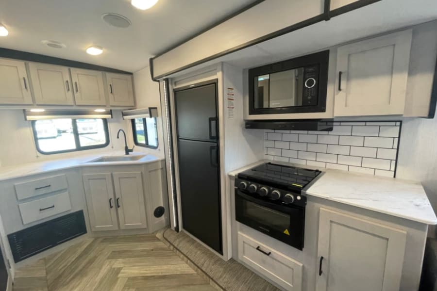 Modern RV rental kitchen with light cabinets, white countertops, black appliances, and subway tile backsplash.