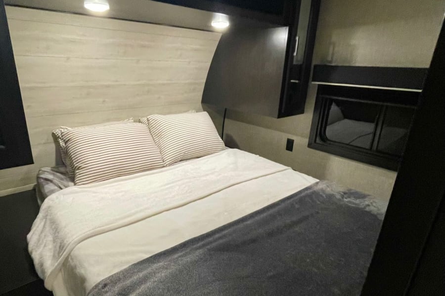 Cozy RV rental bedroom with a made-up bed, striped pillows, and dark overhead cabinets.