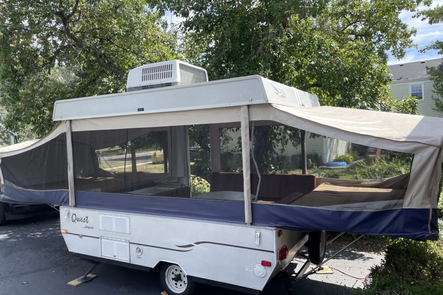 A spacious pop-up camper, perfect for an RV rental, set up with mesh windows & extended beds under trees.