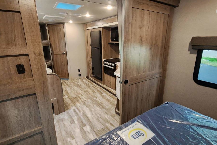 RV rental interior: A bright, spacious view of the kitchen, bed, and living area, featuring wood cabinetry and skylights.
