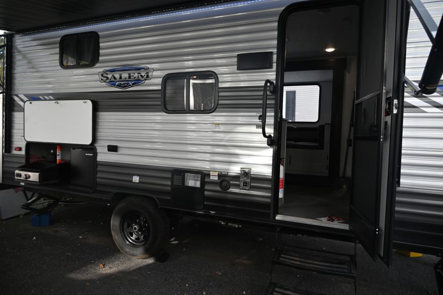 Salem FSX travel trailer: outdoor kitchen, open door, and awning visible. Ideal for an RV rental adventure.