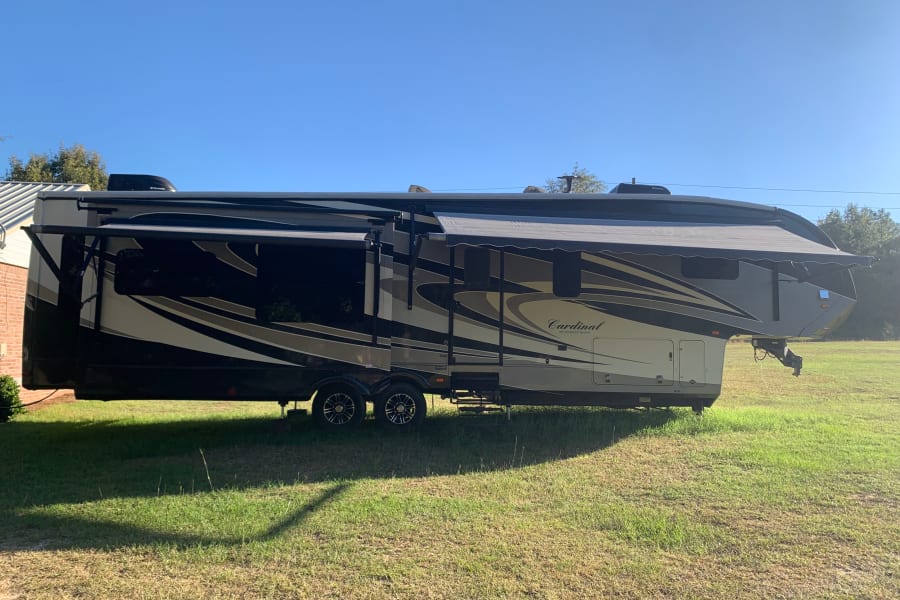 This large Cardinal fifth-wheel RV is parked with its awnings extended in a sunny, grassy outdoor setting, perfect for an RV rental.