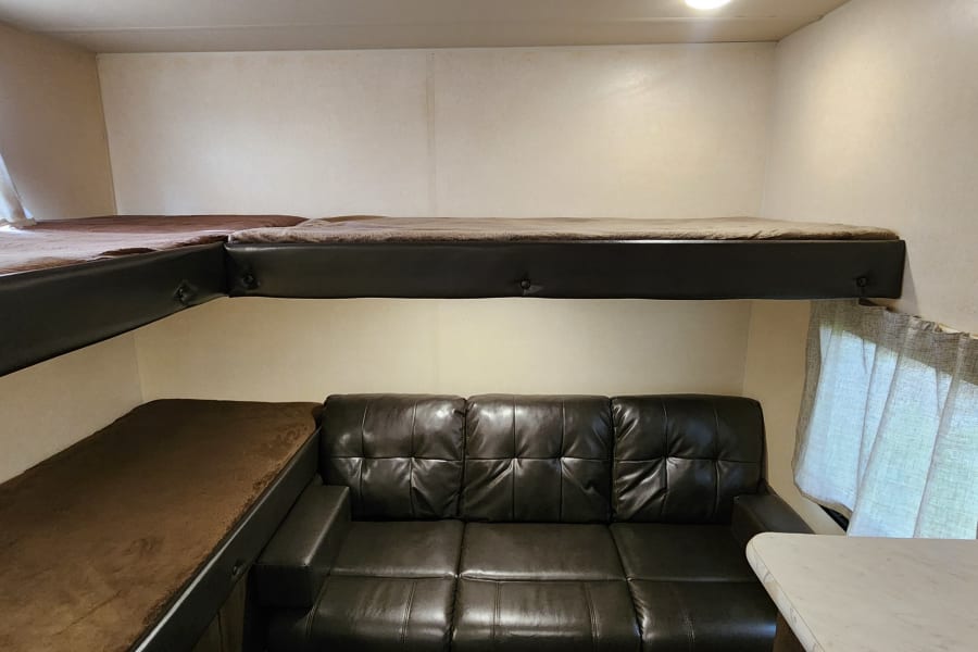 RV rental interior: a cozy living space featuring three brown bunk beds and a dark leather sofa, ideal for group comfort.