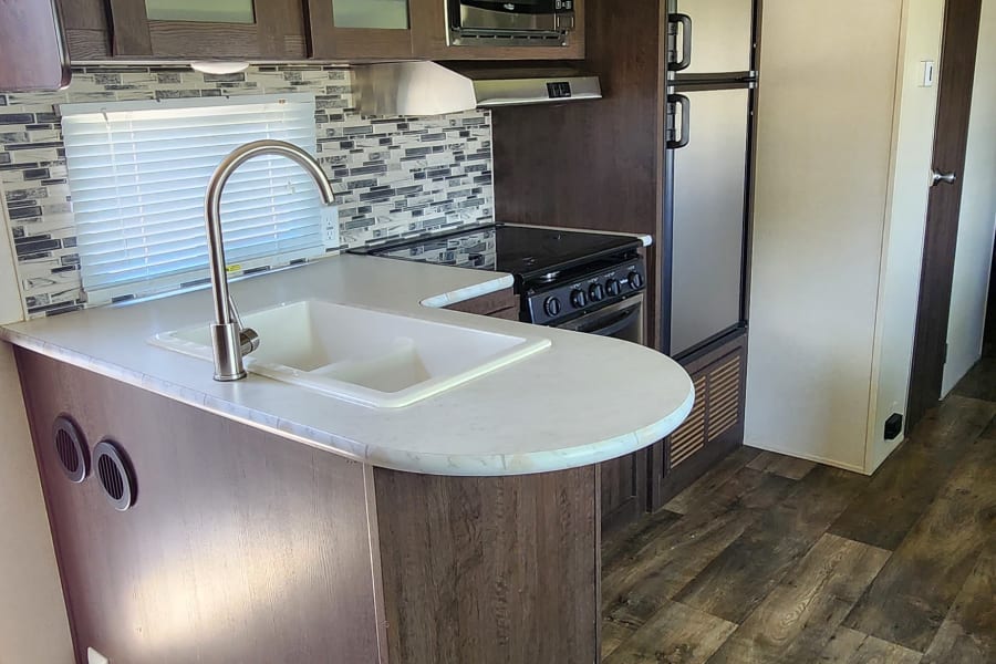 Well-appointed RV rental interior showcasing a full kitchen with modern appliances and wood-look flooring.