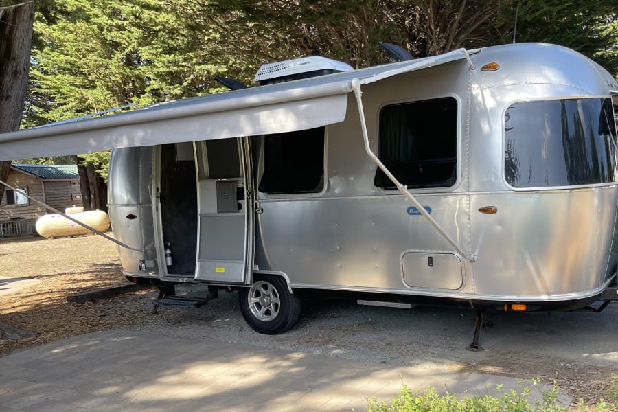 A stylish Airstream travel trailer with its door open and awning out, ready for your next rv rental camping trip.