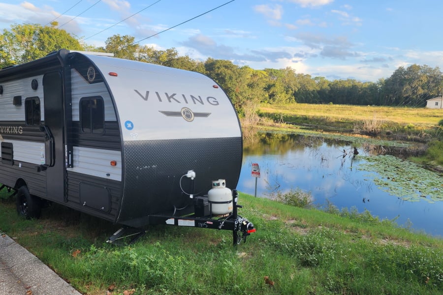 Viking travel trailer, ideal for an RV rental, parked roadside by a tranquil pond with lily pads.